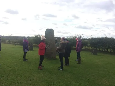 A group of retreat guests gathered around a standing stone in a field
